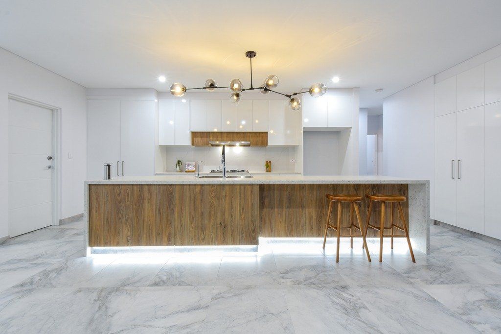 A kitchen with white cabinets , a wooden island , and a marble floor.