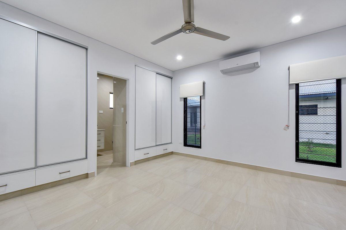 A large empty room with a ceiling fan and two windows.