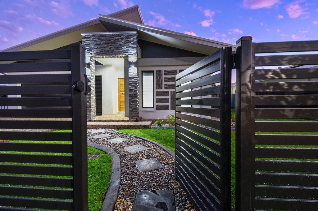 A black fence is open to a house with a path leading to it.