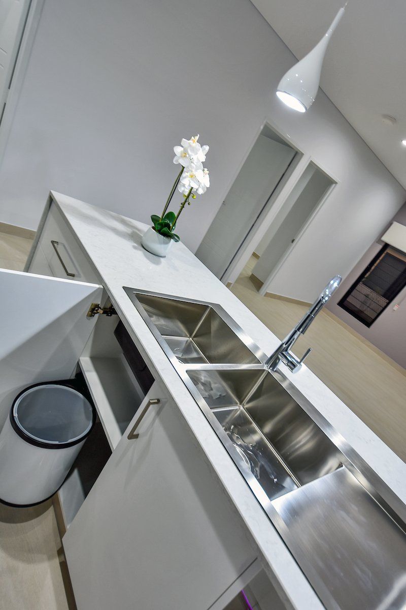 A kitchen with a stainless steel sink and a trash can