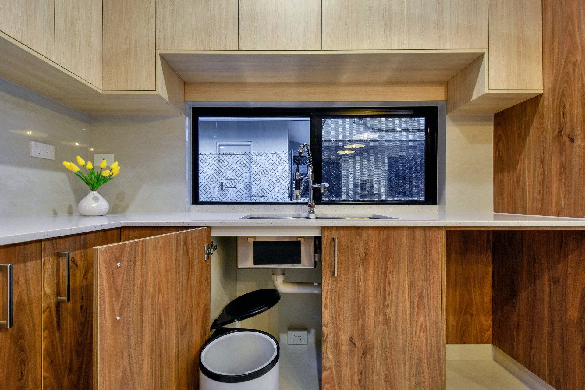 A kitchen with wooden cabinets and a trash can under the sink.