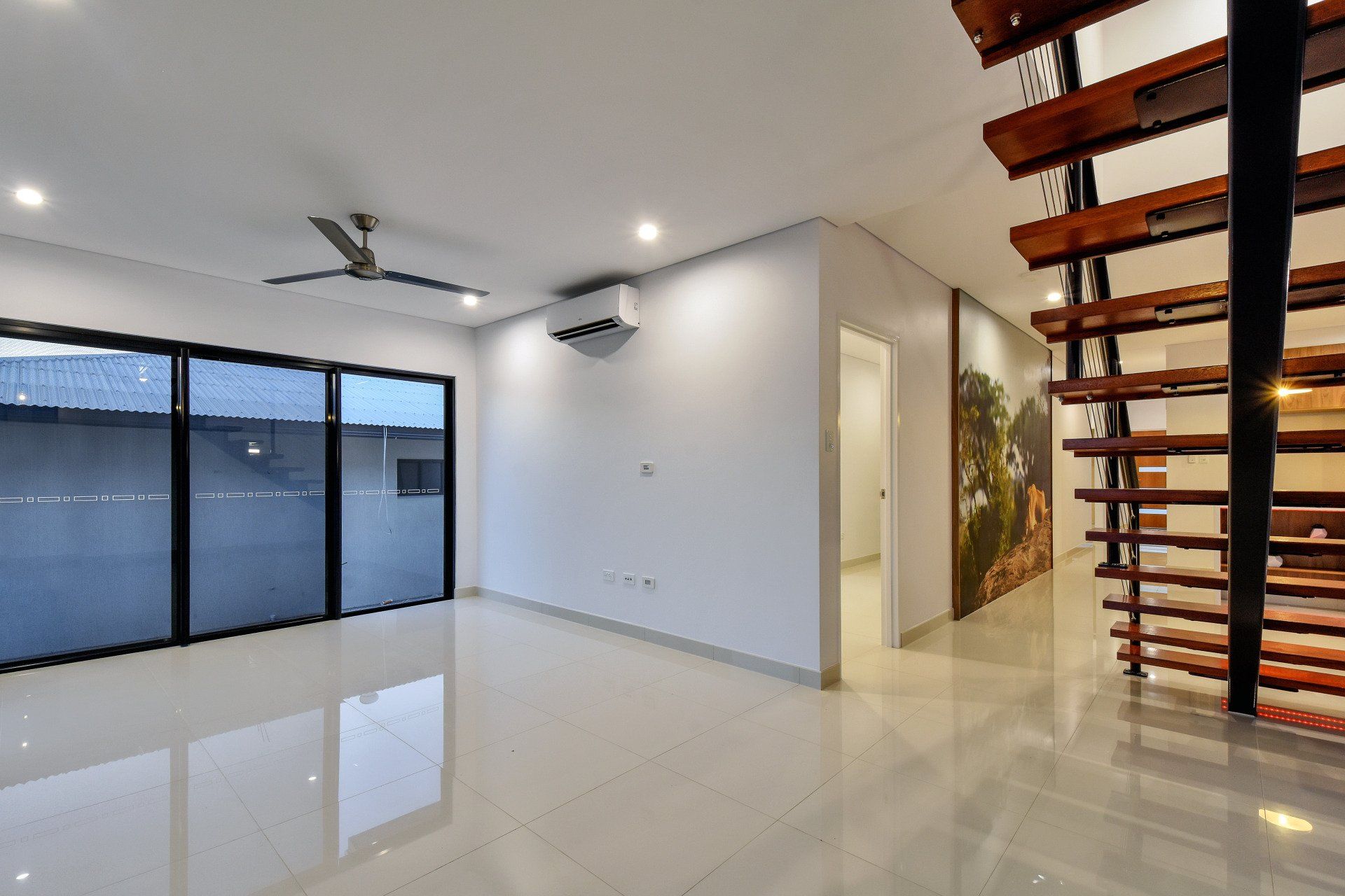 An empty living room with a ceiling fan and stairs