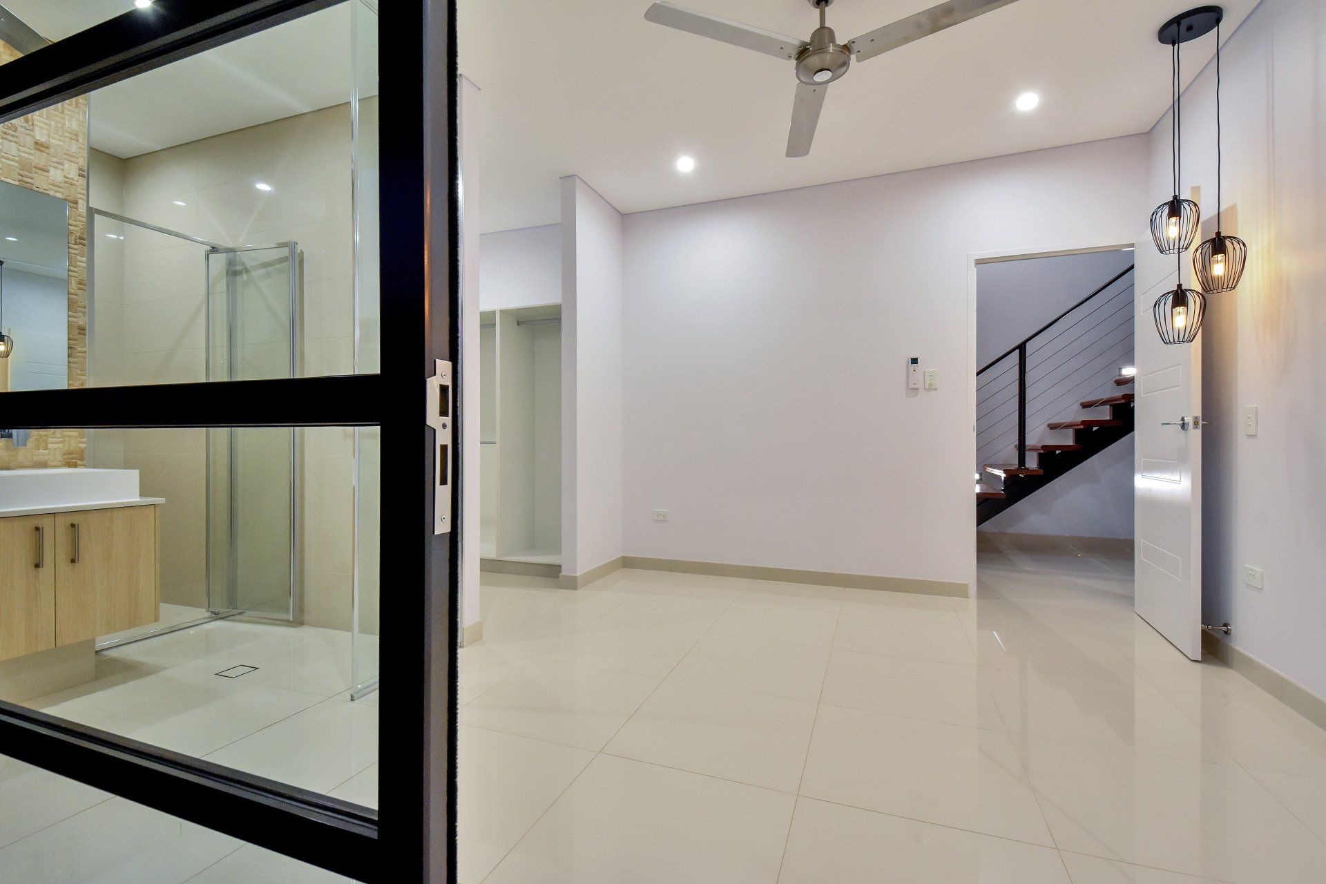 An empty room with a ceiling fan and a bathroom in the background.