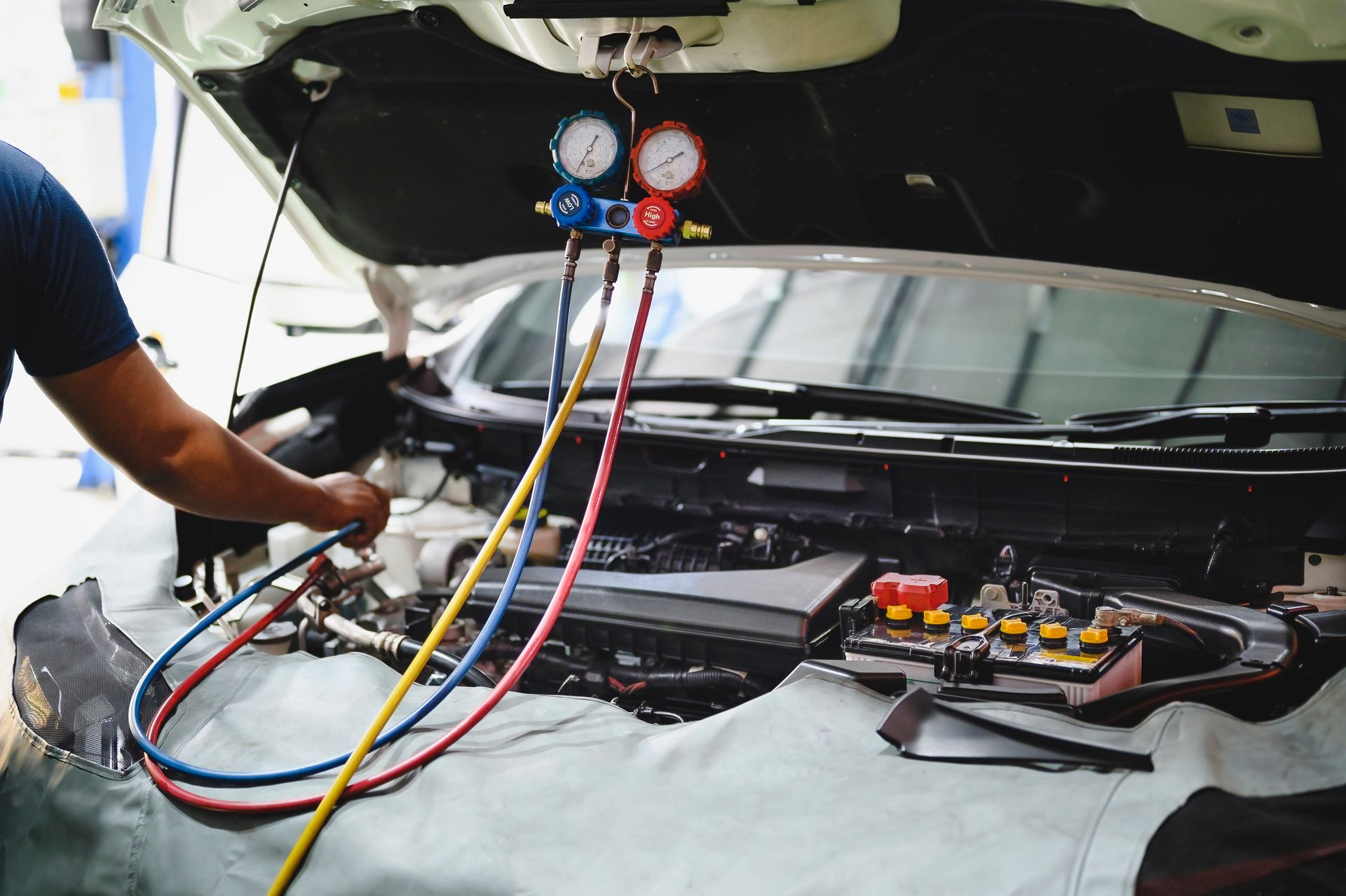 Mechanic servicing car's AC system with gauges and hoses in an engine bay.| Mountain Automotive and Performance