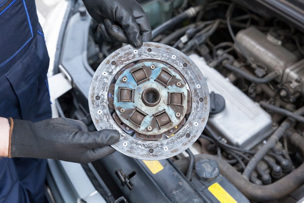 A Person Is Holding A Clutch Disc In Front Of A Car Engine — Goodyear Autocare Bowen in Bowen, QLD