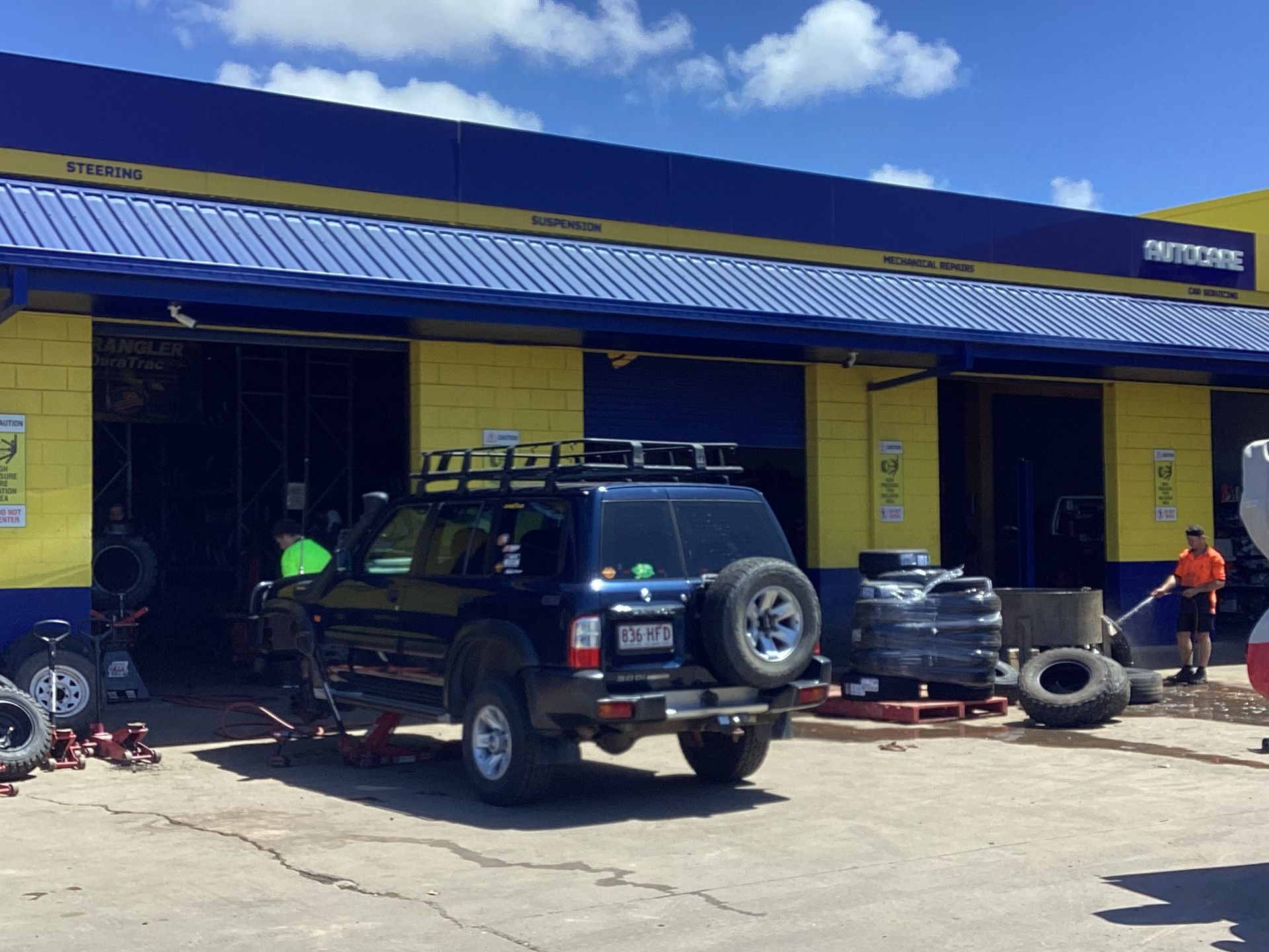 A Man Is Working On A Car Underneath It In A Garage — Goodyear Autocare Bowen in Bowen, QLD