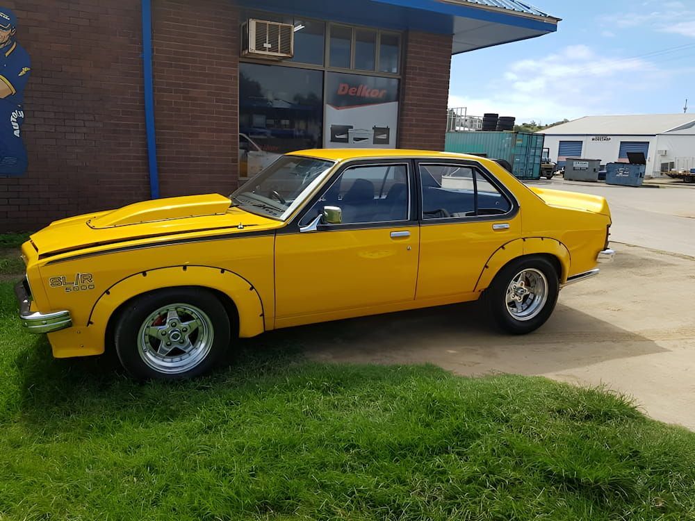 A Yellow Car Is Parked In Front Of A Brick Building — Goodyear Autocare Bowen in Bowen, QLD