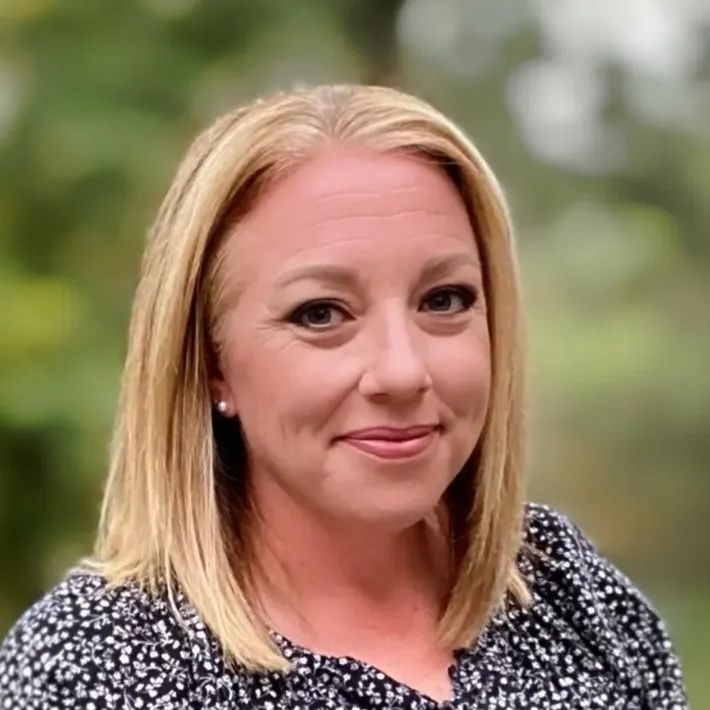 A woman with blonde hair is smiling for the camera while wearing a black and white polka dot shirt.