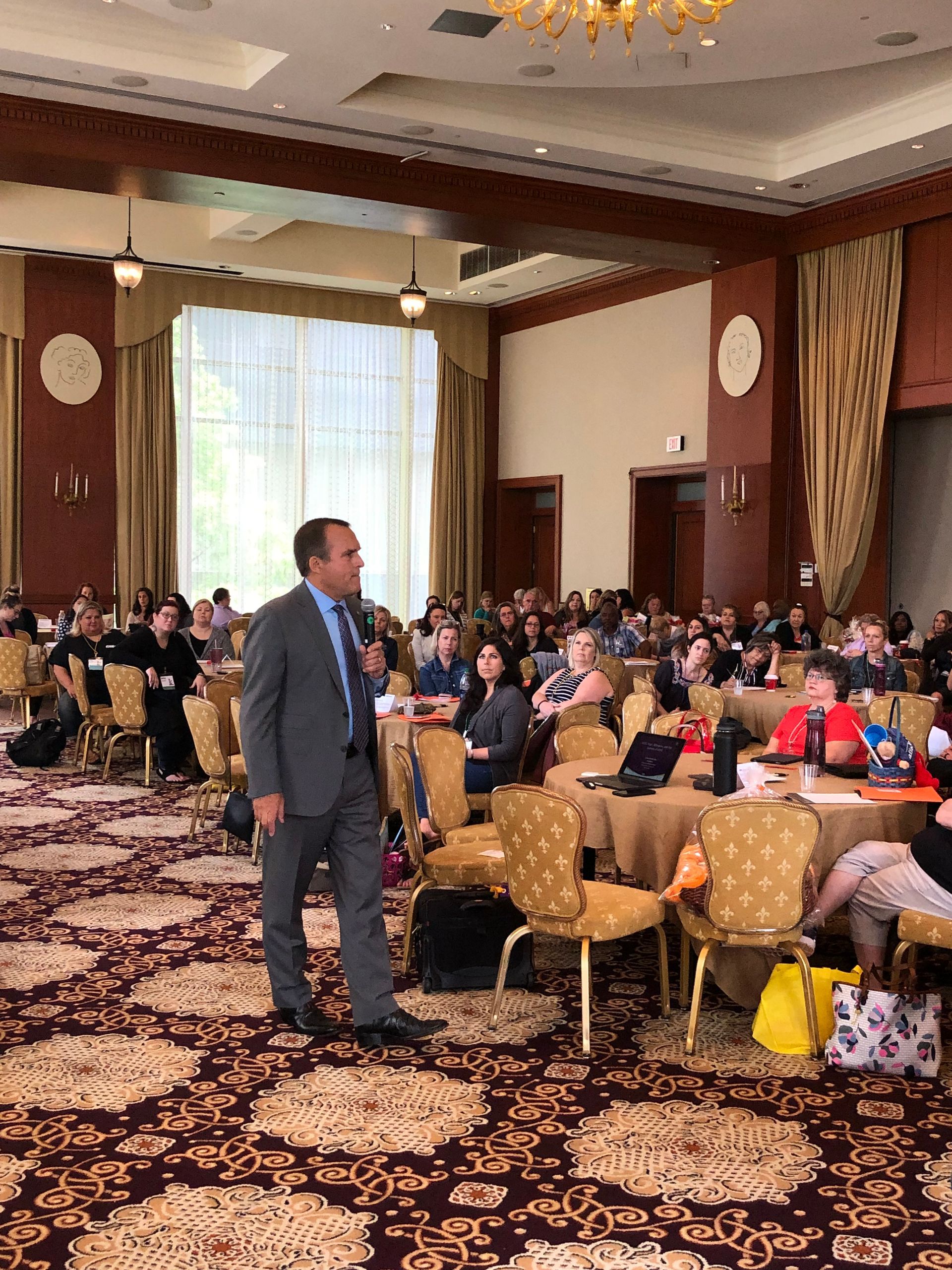 A man in a suit is standing in front of a crowd of people in a large room.