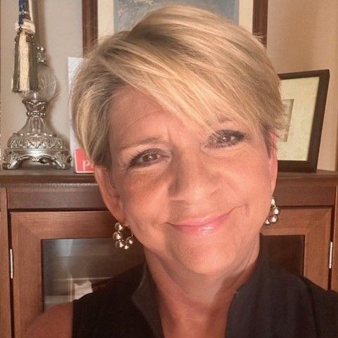 A woman with short blonde hair and earrings is smiling for the camera.