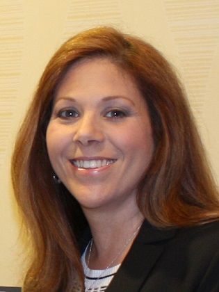 A woman with long red hair is smiling and wearing a black jacket