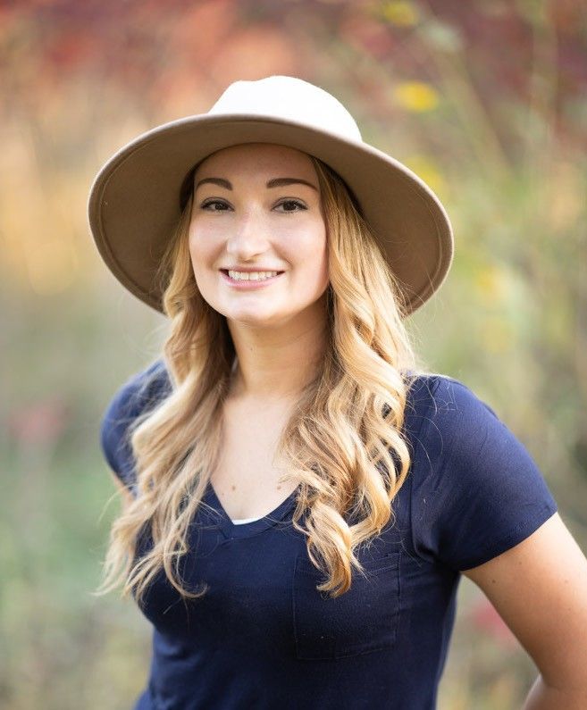 A woman wearing a hat and a blue shirt is smiling for the camera.