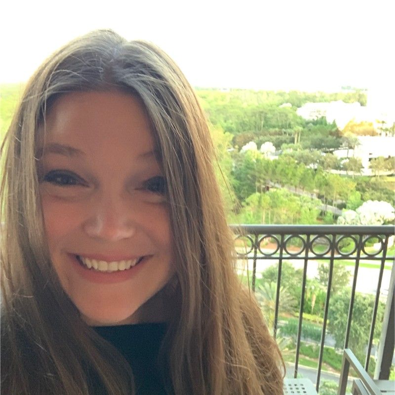 A woman with long hair is smiling in front of a balcony
