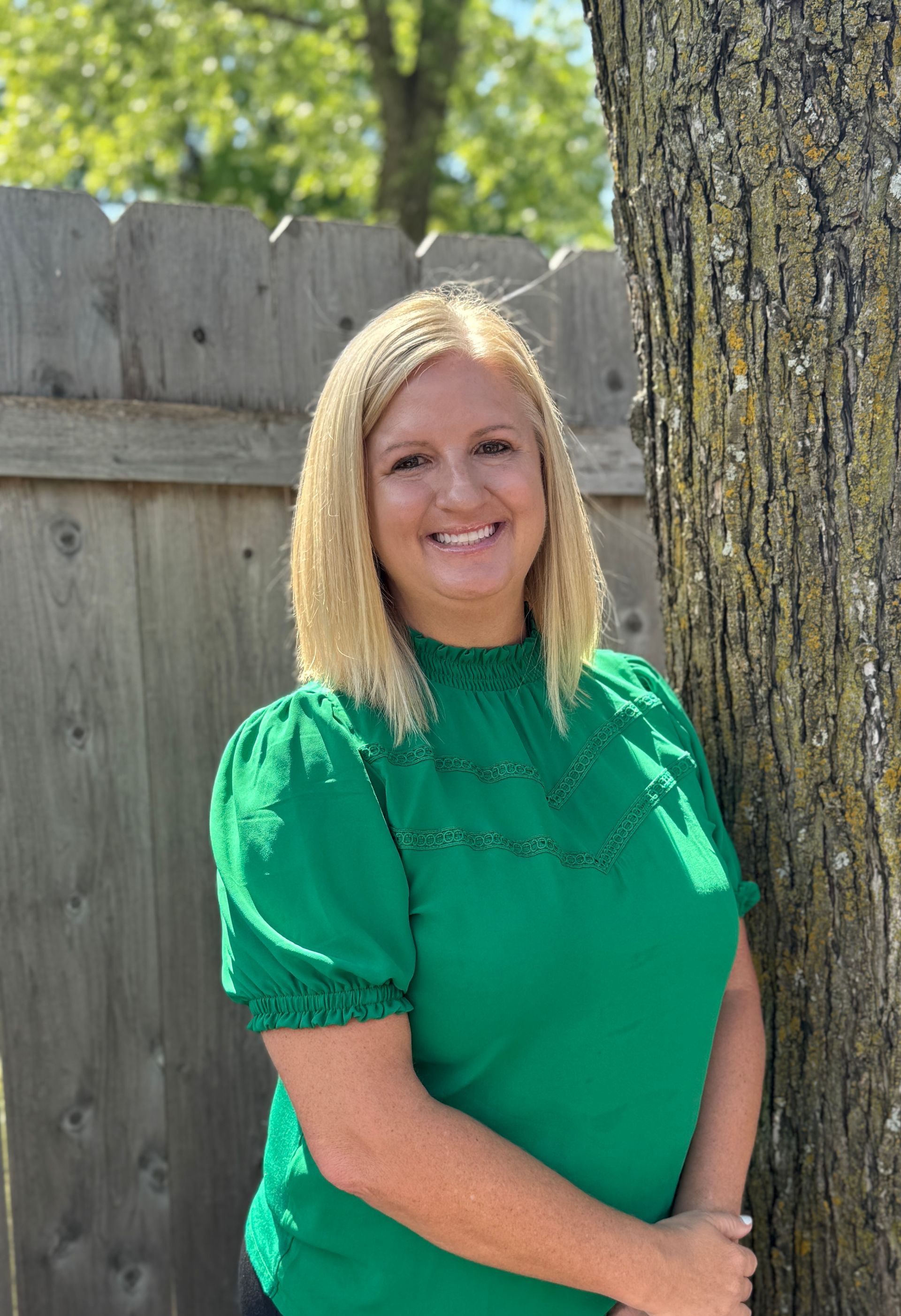 A woman in a green shirt is standing next to a tree.