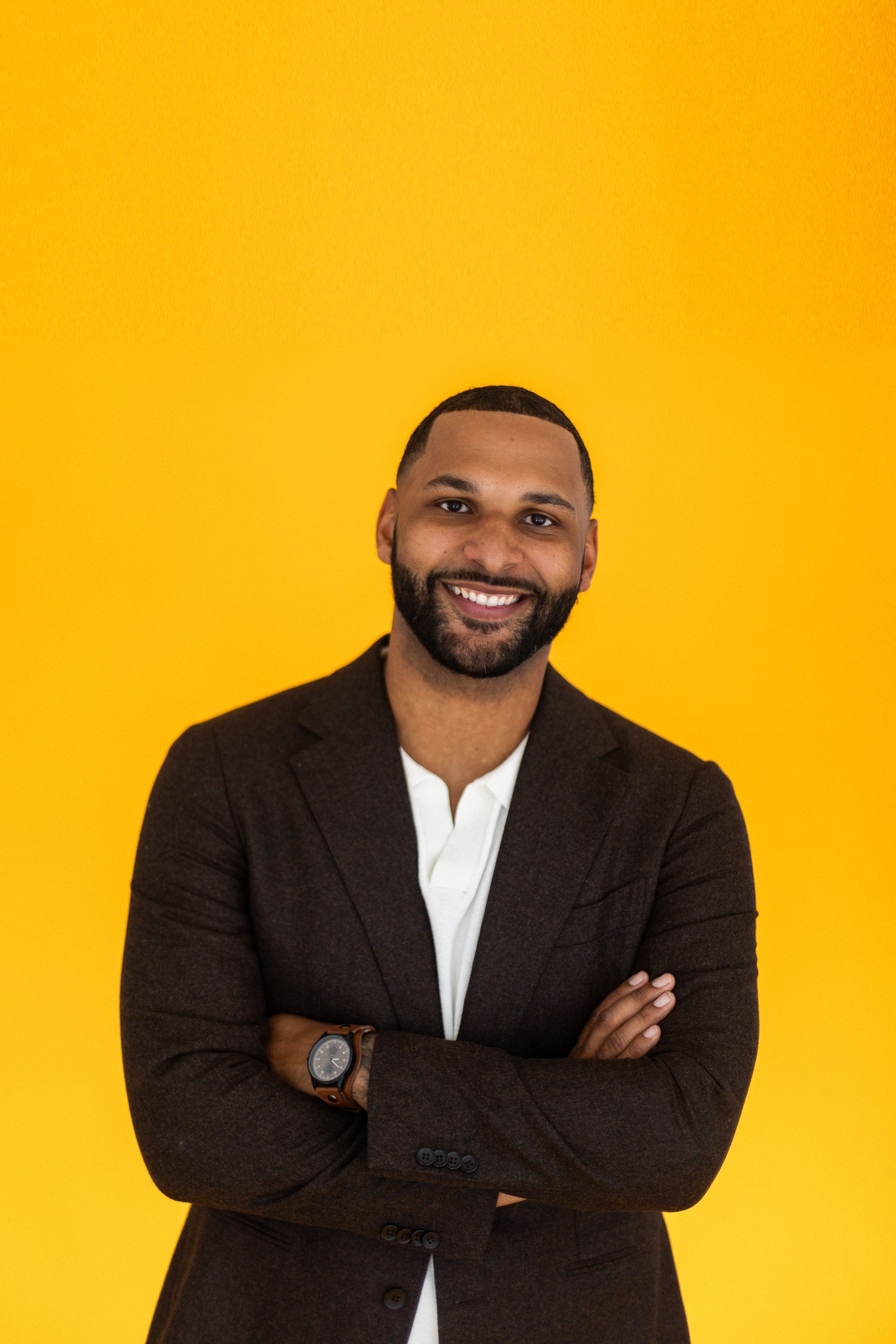 A man in a suit is standing with his arms crossed and smiling.