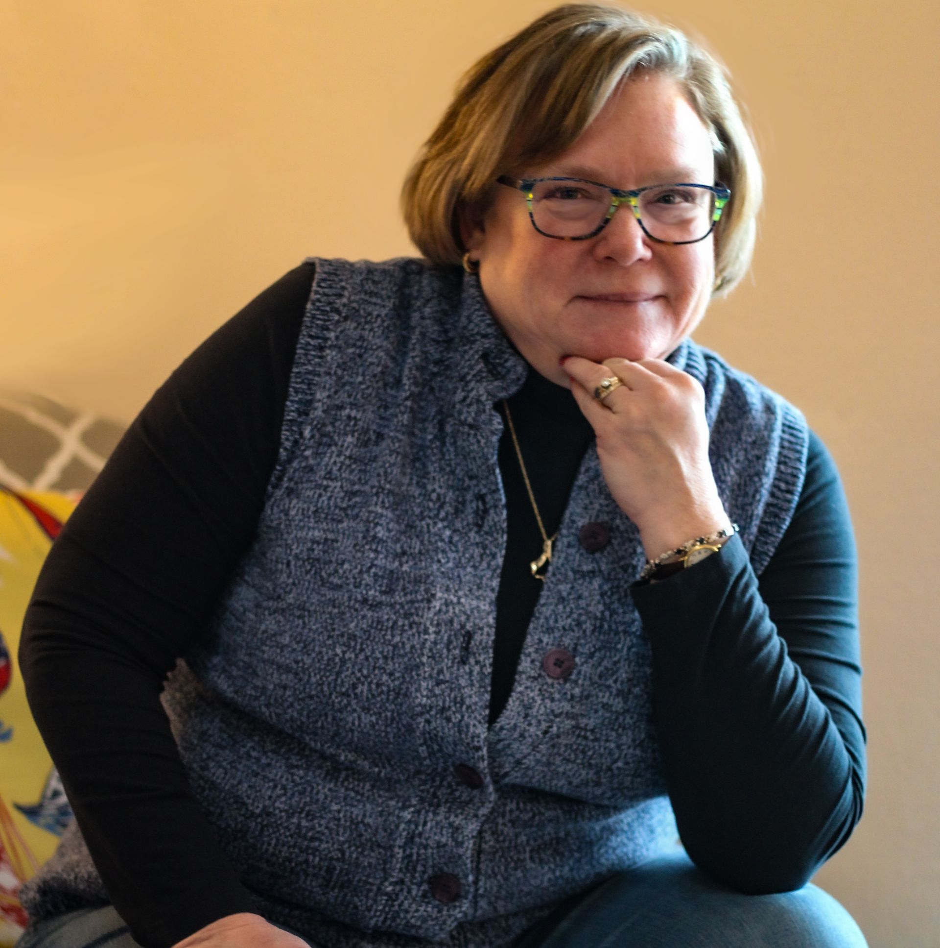 A woman wearing glasses and a vest is sitting on a couch
