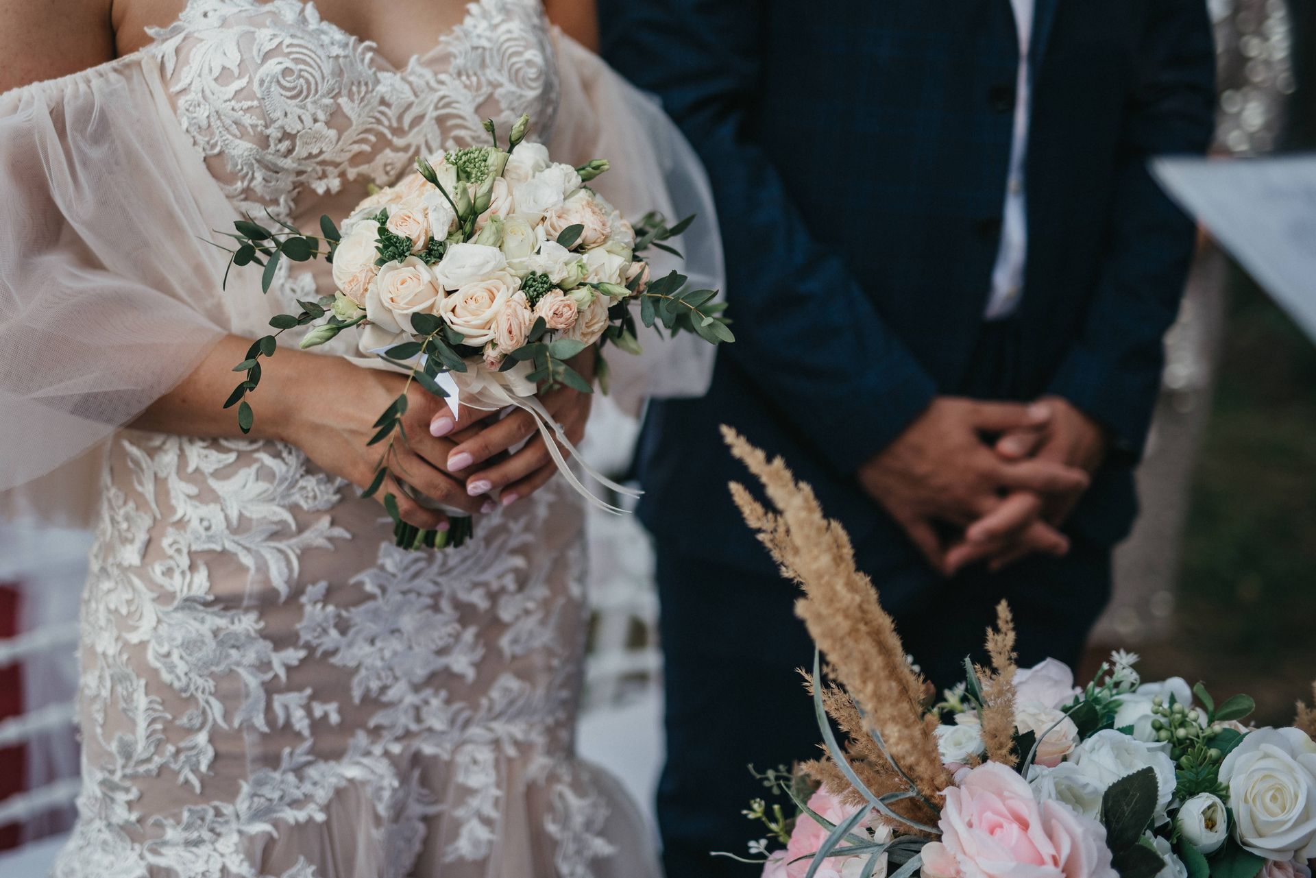 Una sposa tiene in mano un mazzo di fiori mentre è in piedi accanto allo sposo.