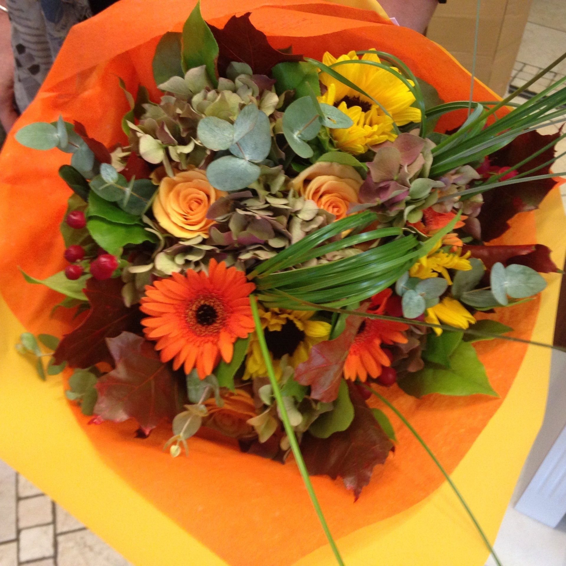 Una persona tiene in mano un mazzo di fiori avvolto in carta arancione