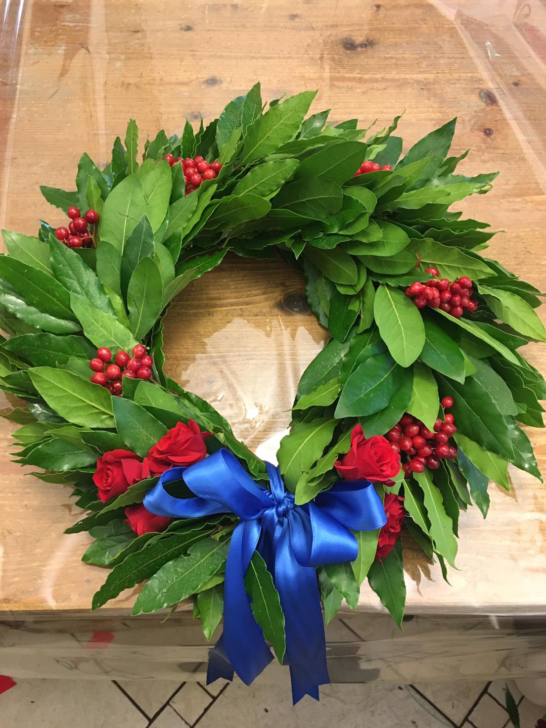 Una corona con bacche rosse e un fiocco blu su un tavolo di legno