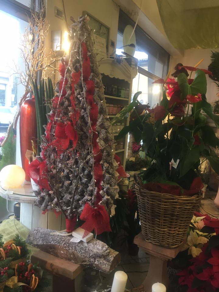 Un albero di Natale è appoggiato su un tavolo in una stanza, circondato da fiori e candele.