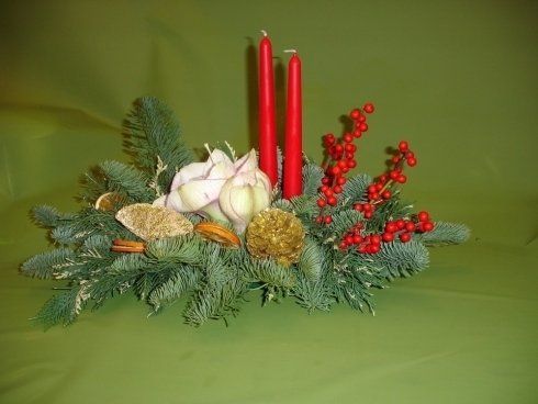 Un centrotavola natalizio con candele rosse e fiori su un tavolo verde.