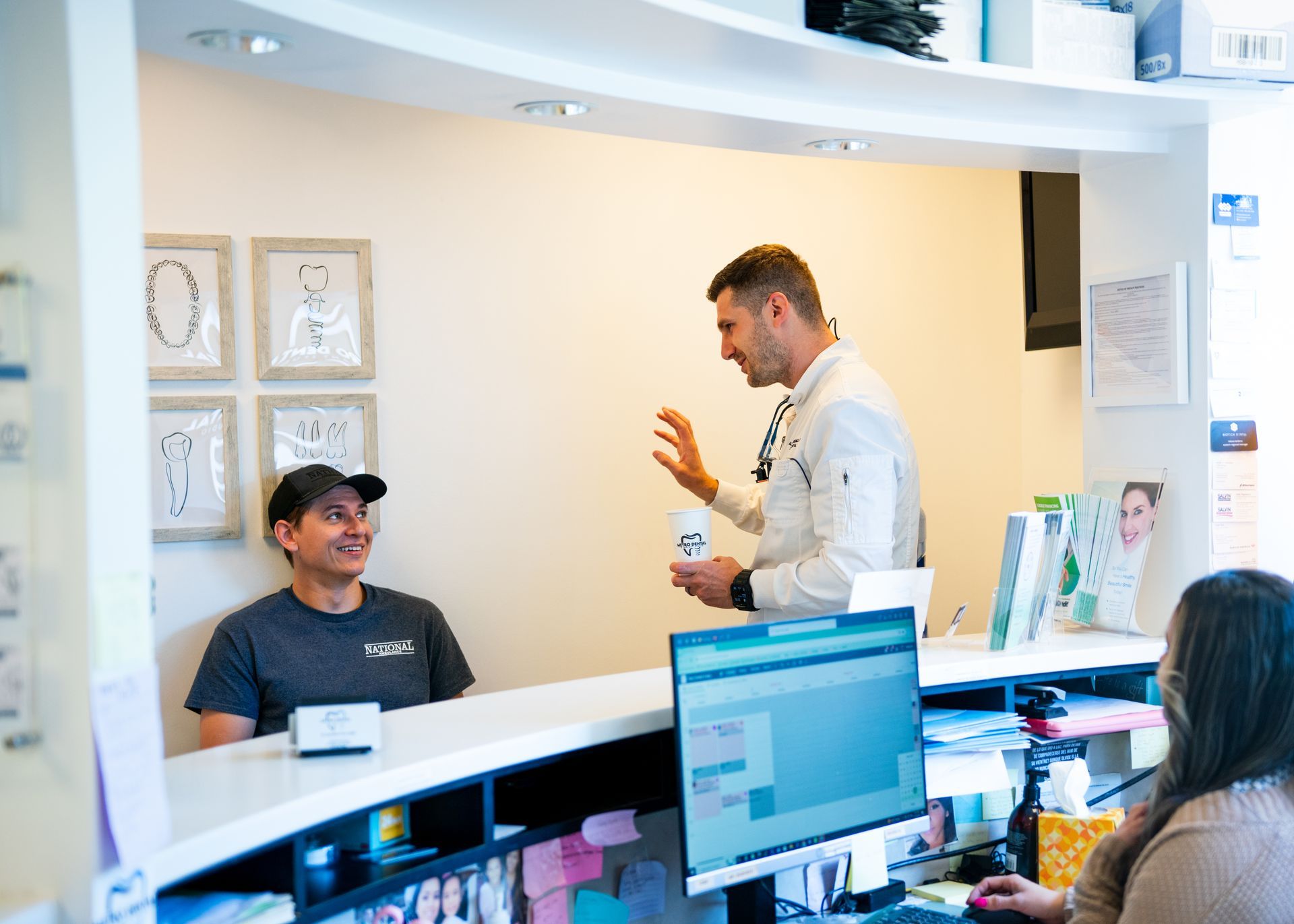 A man is sitting at a counter in a dental office talking to a doctor.