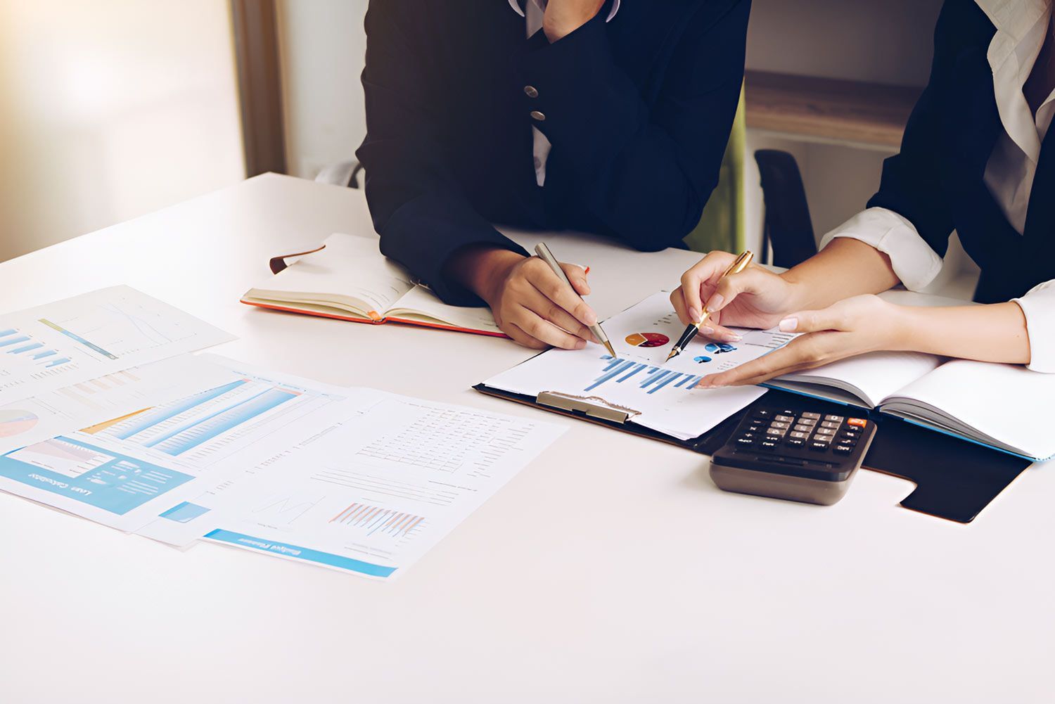 Two Women Are Sitting At A Table With Papers And A Calculator — Whitson Dawson Accountants in Mackay, QLD