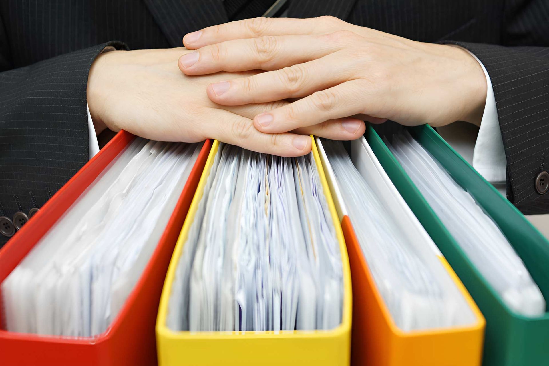 A Person Is Holding A Stack Of Binders With Their Hands — Whitson Dawson Accountants in Mackay, QLD