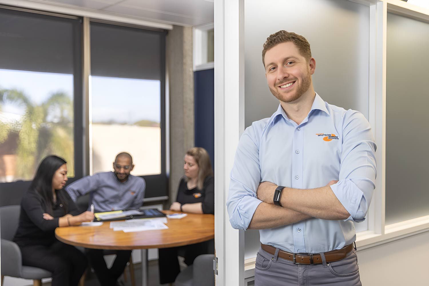 A Man Is Standing In A Room With His Arms Crossed In Front Of A Group Of Auditor — Whitson Dawson Accountants in Mackay, QLD