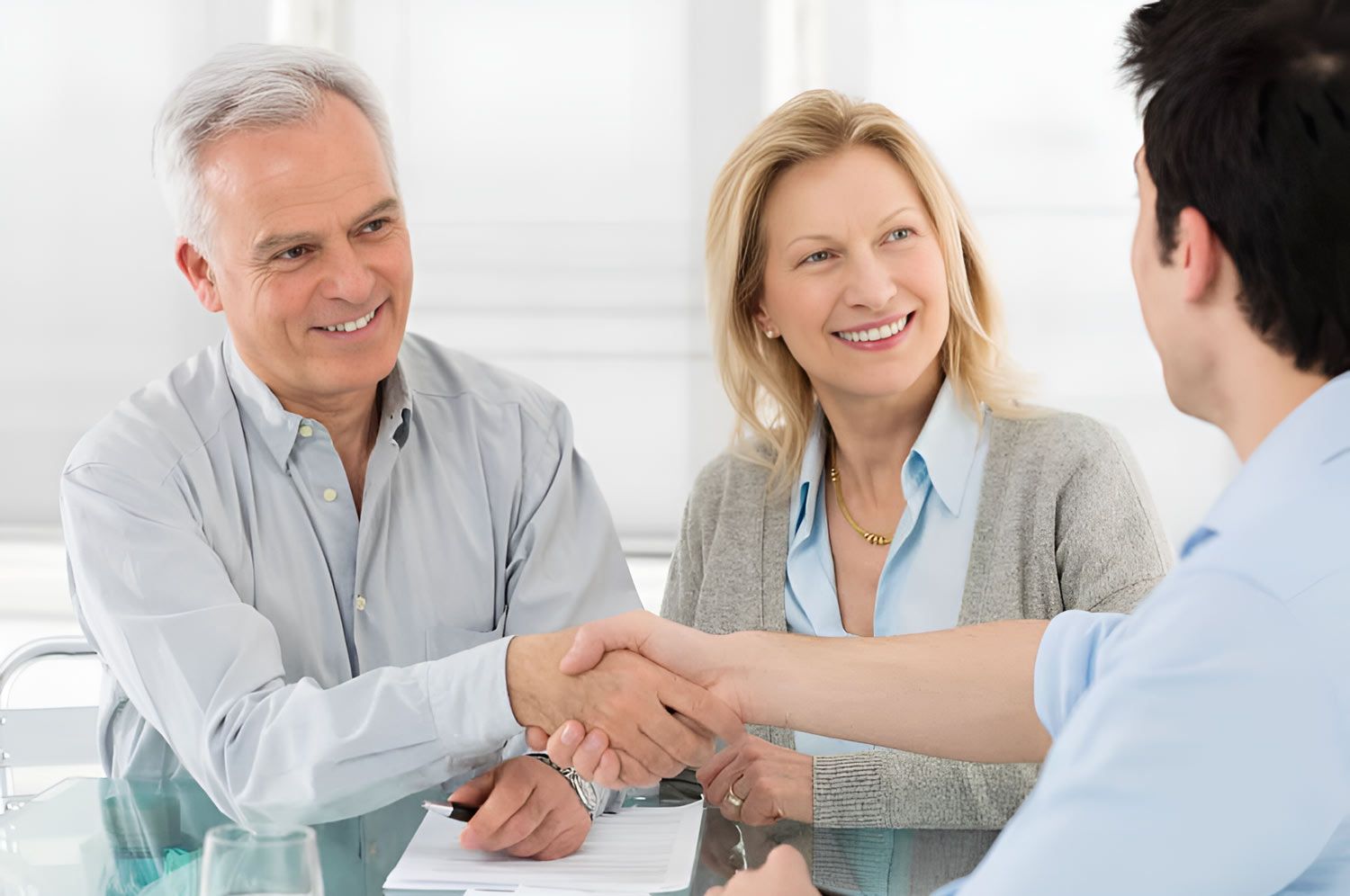 A Man And Woman Are Shaking Hands While Sitting At A Table — Whitson Dawson Accountants in Central Queensland