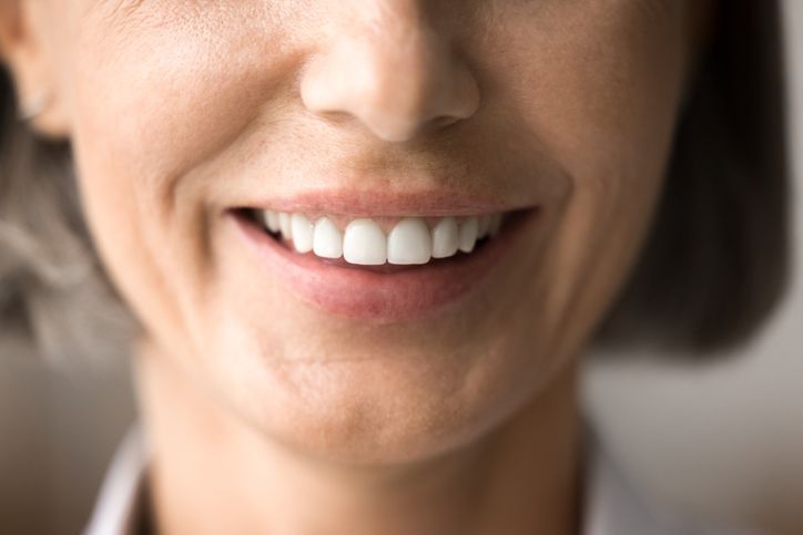 Close-up of a smiling mouth and nose with white teeth in soft light