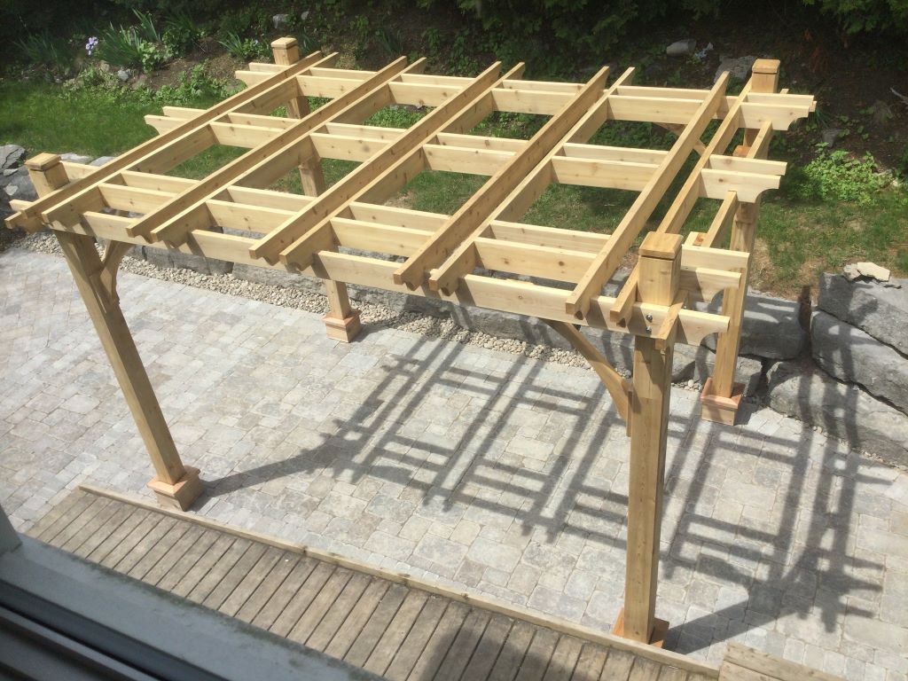 A wooden pergola is in the backyard of a house.