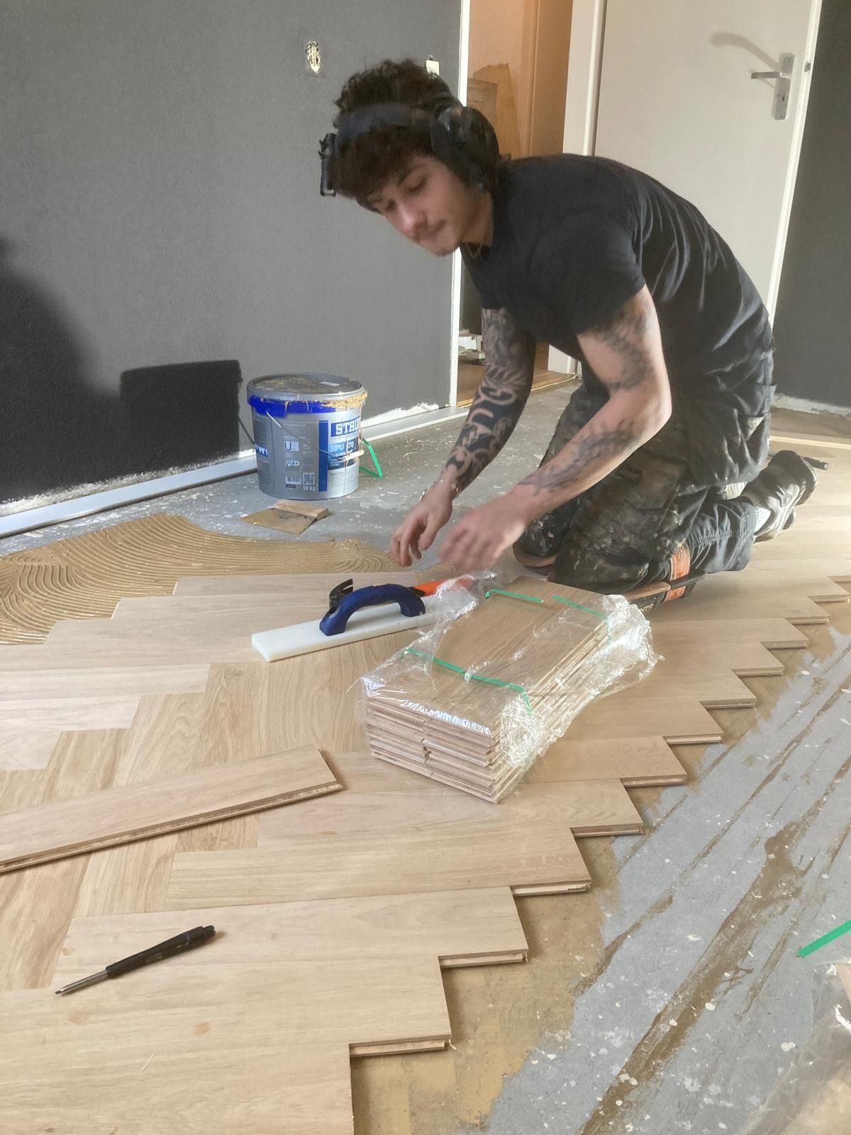 Een man knielt op de grond en werkt op een houten vloer.