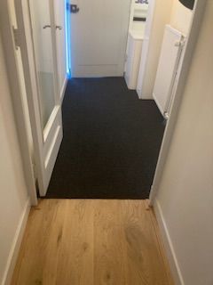 Een gang met hardhouten vloer en zwart tapijt.