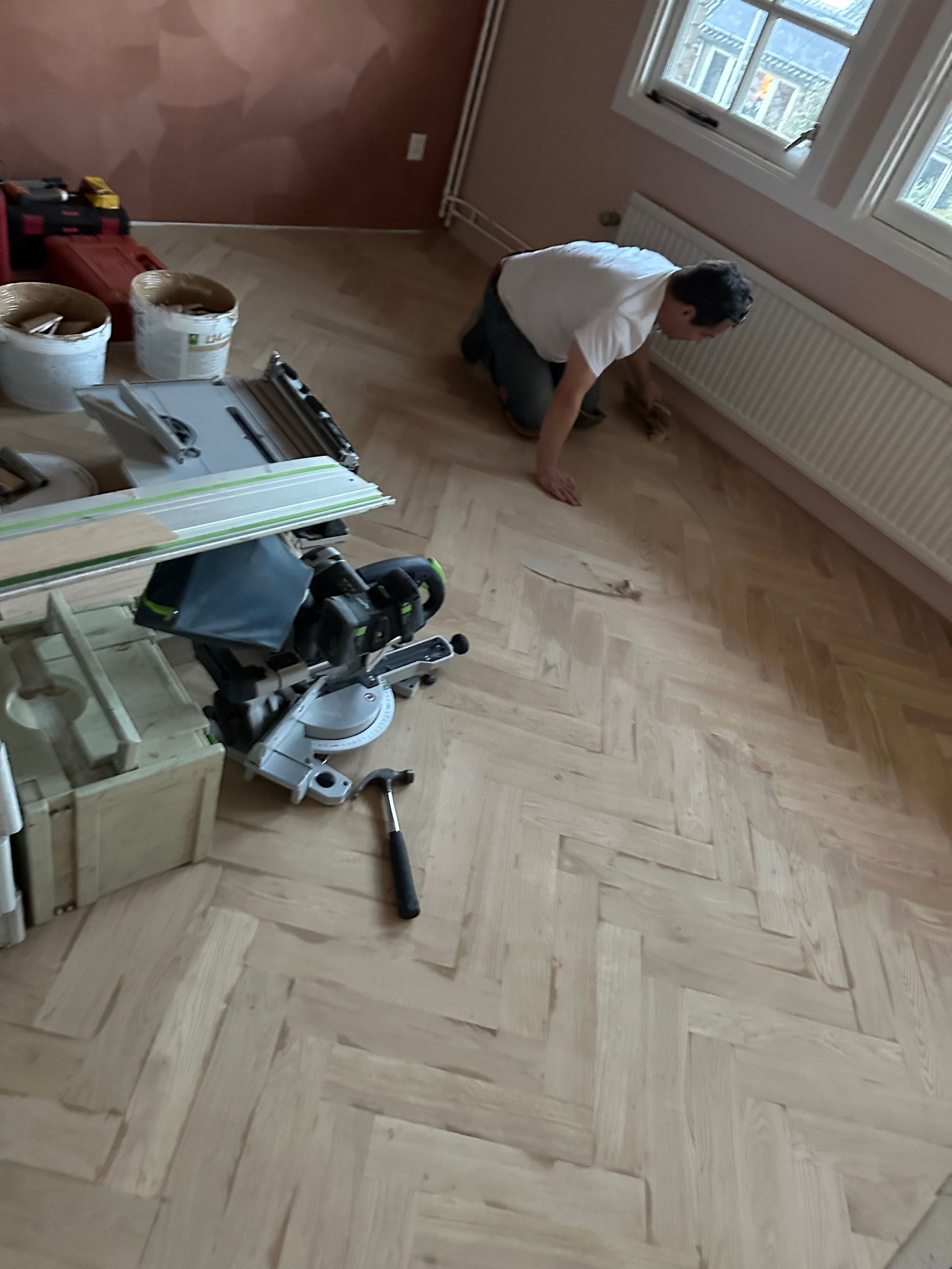 Een man knielt op een houten vloer in een kamer.