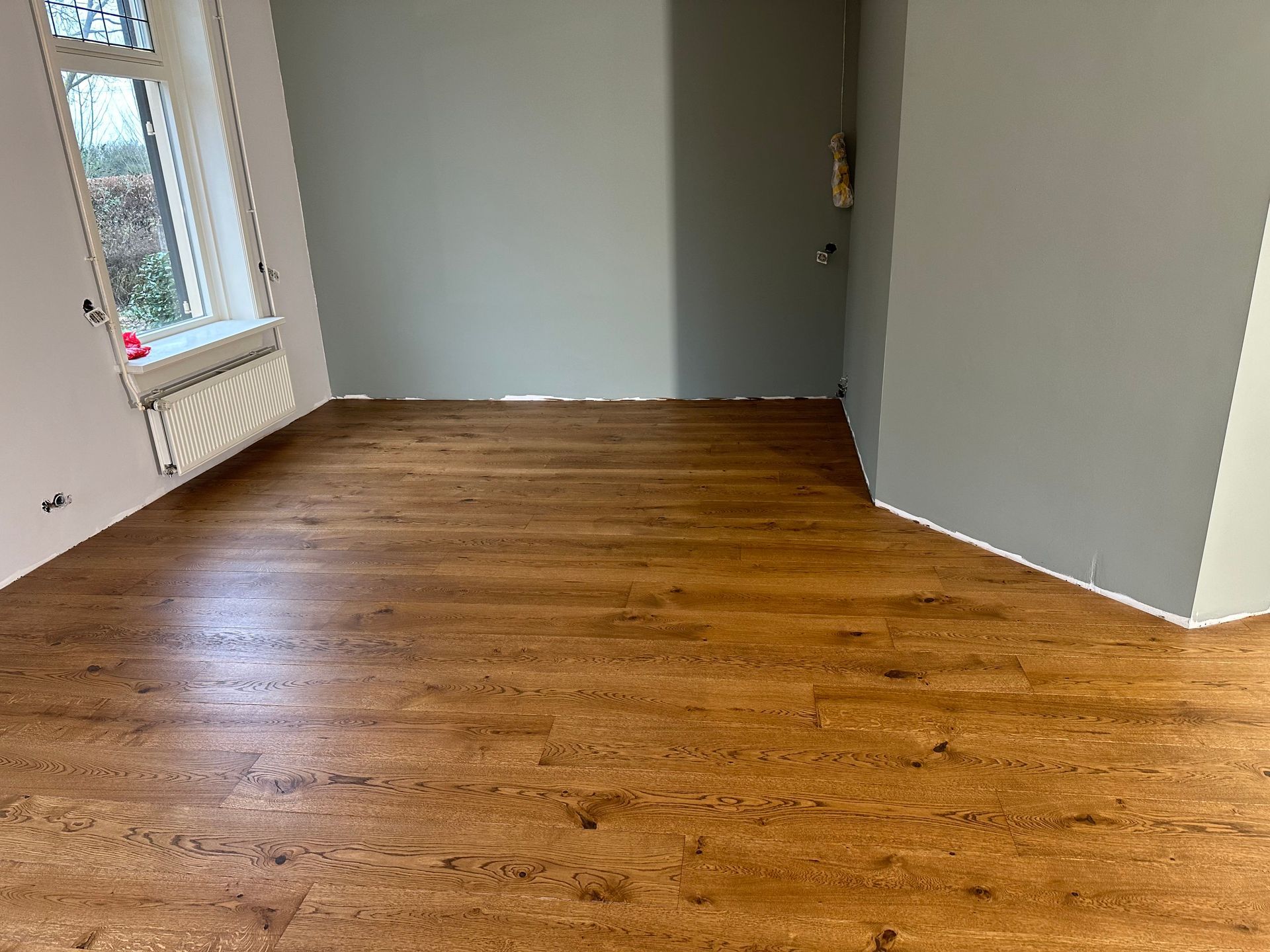 Een lege kamer met een houten vloer en een raam.