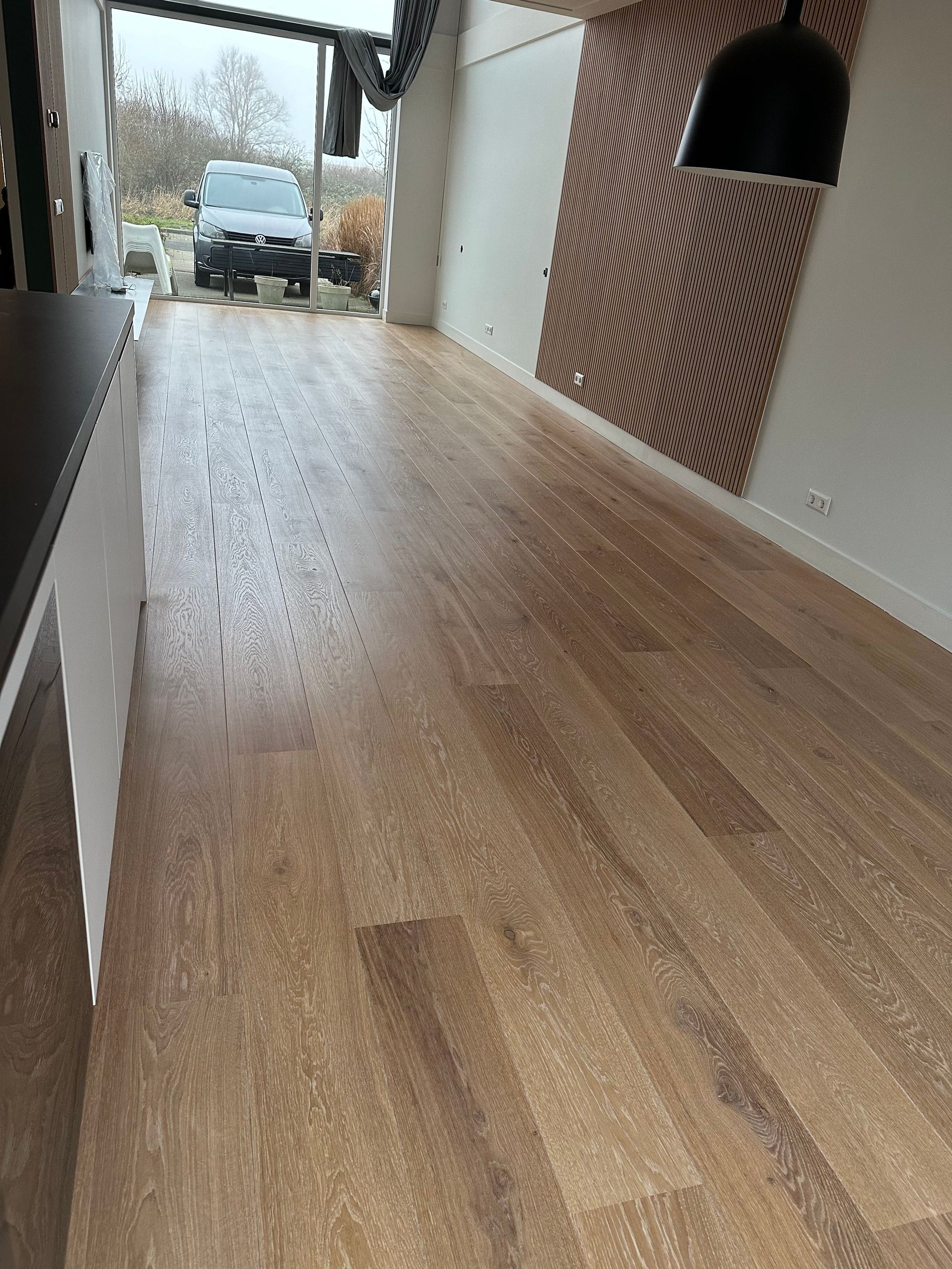 Een woonkamer met een houten vloer en een auto geparkeerd in de garage.
