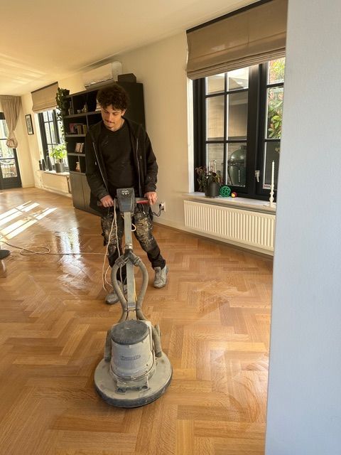 Een man gebruikt een machine om een houten vloer in een woonkamer te polijsten.