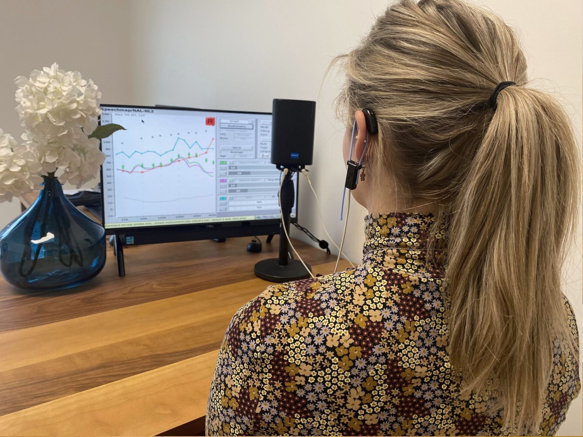 A woman wearing a headset is sitting in front of a computer monitor.