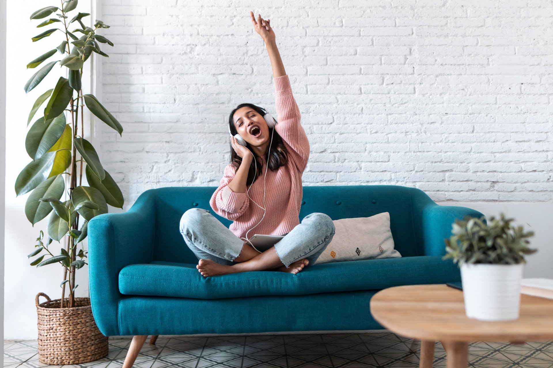 Une femme est assise sur un canapé bleu, portant des écouteurs et écoutant de la musique.