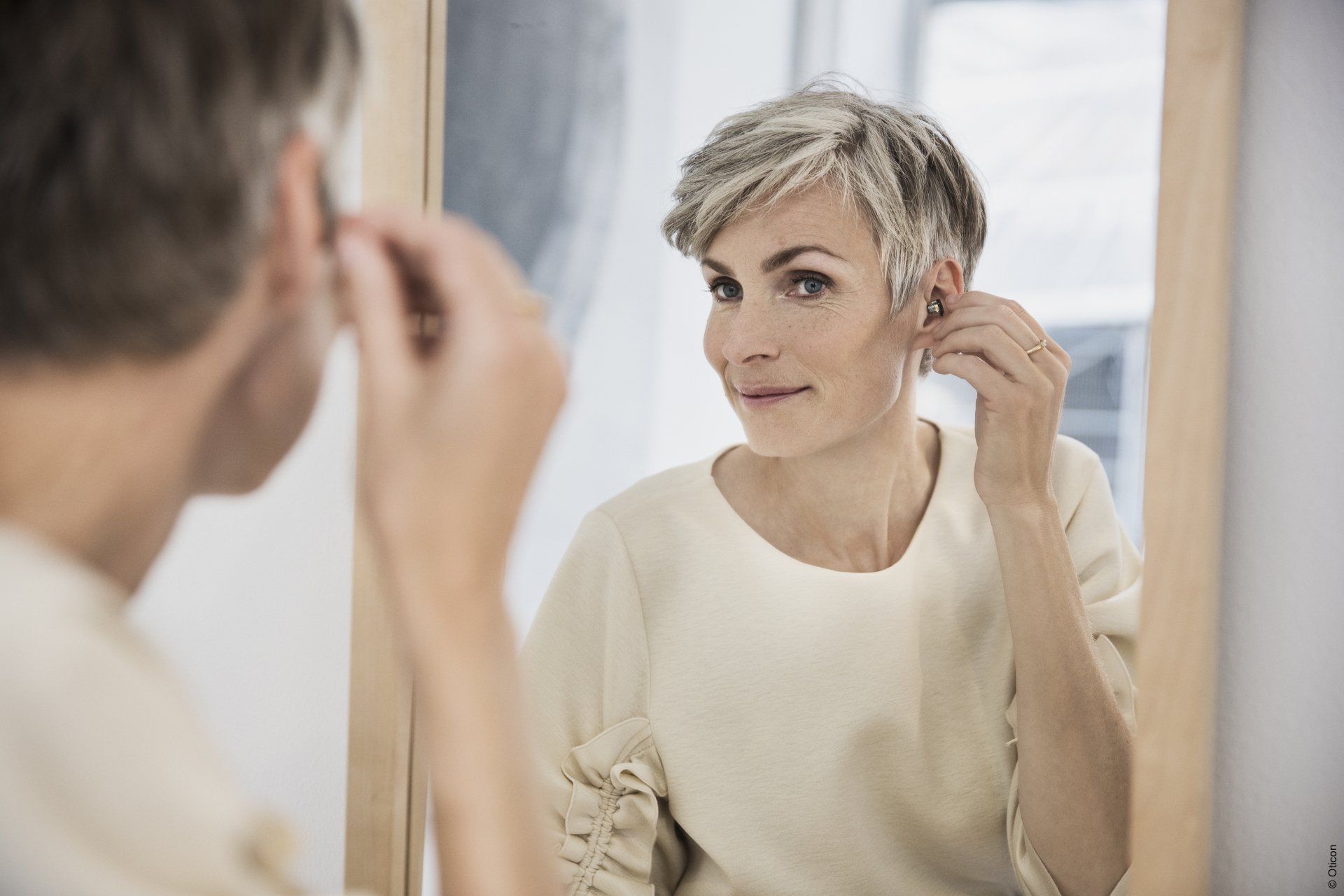 A woman wearing hearing aids is looking at herself in the mirror.
