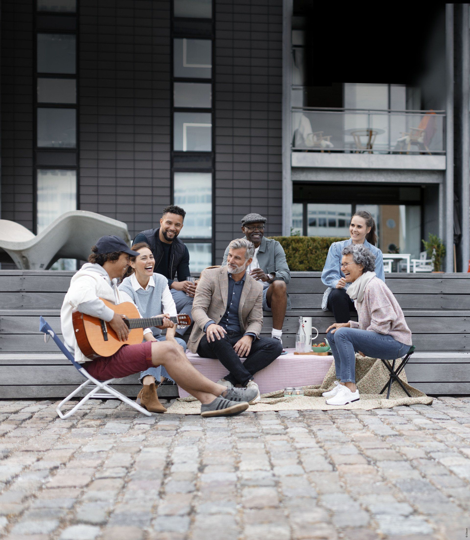 A group of people are sitting around a man playing a guitar.