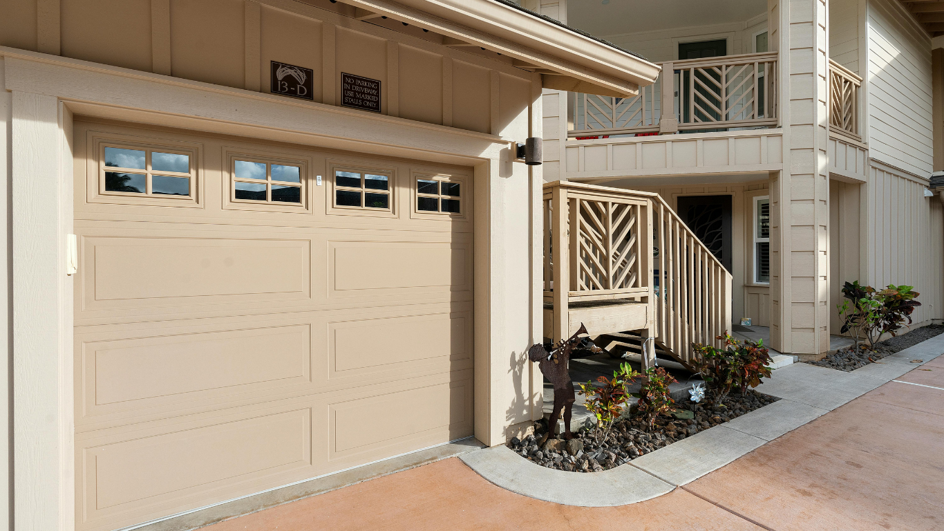 Beige garage door with windows, next to a tan-colored building with a balcony and doorway.