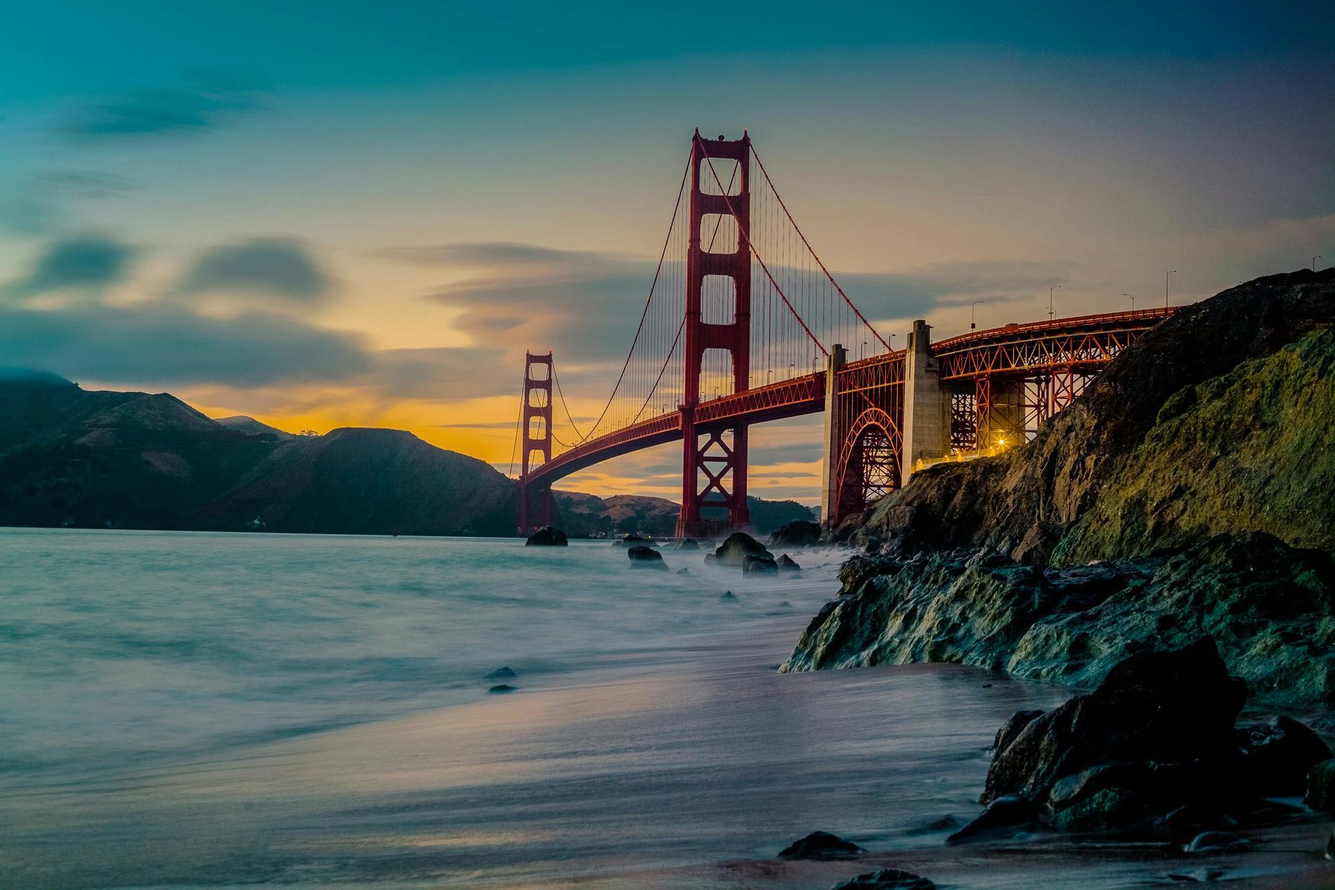 The golden gate bridge is visible from the beach at sunset.