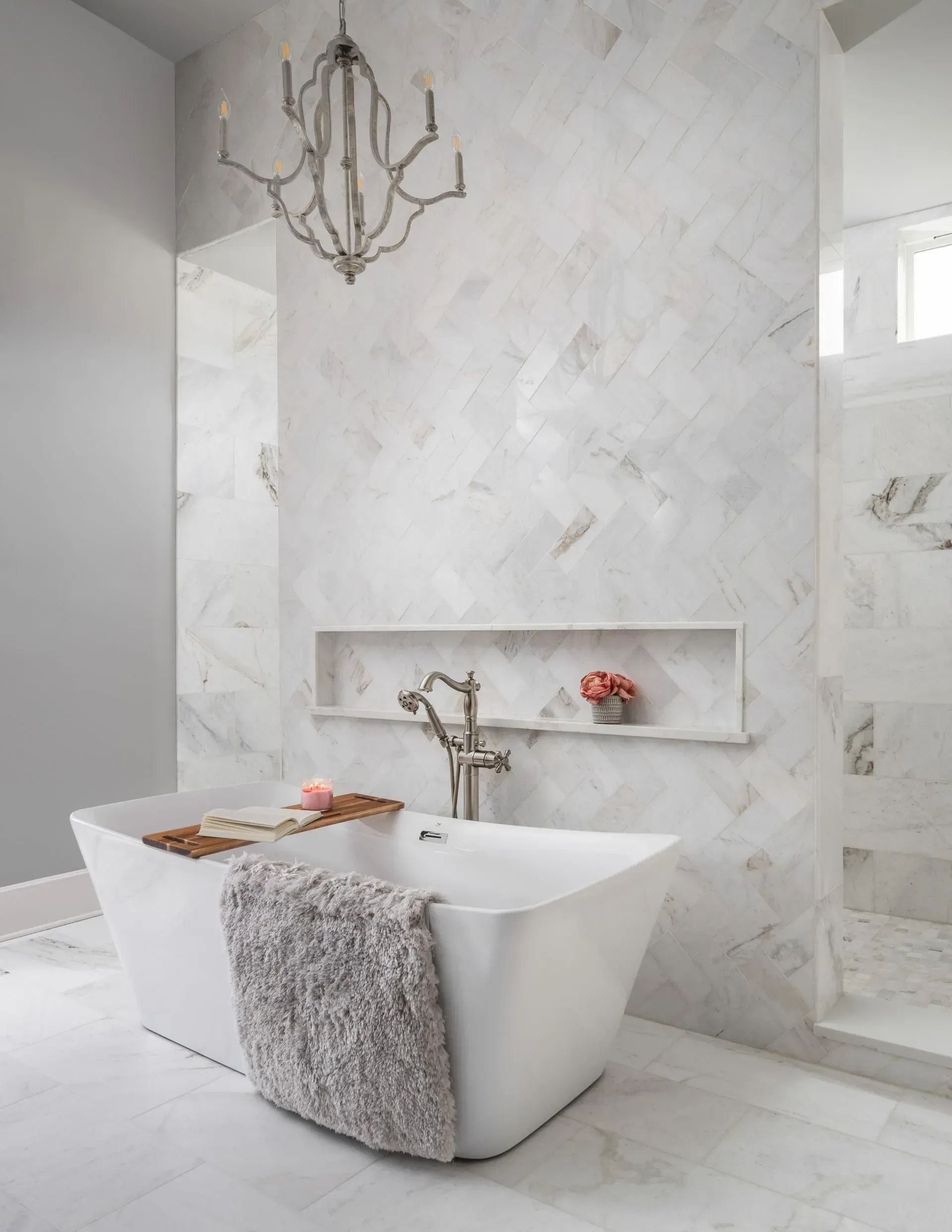 Modern white marble bathroom with freestanding tub, chandelier, and built-in wall niche