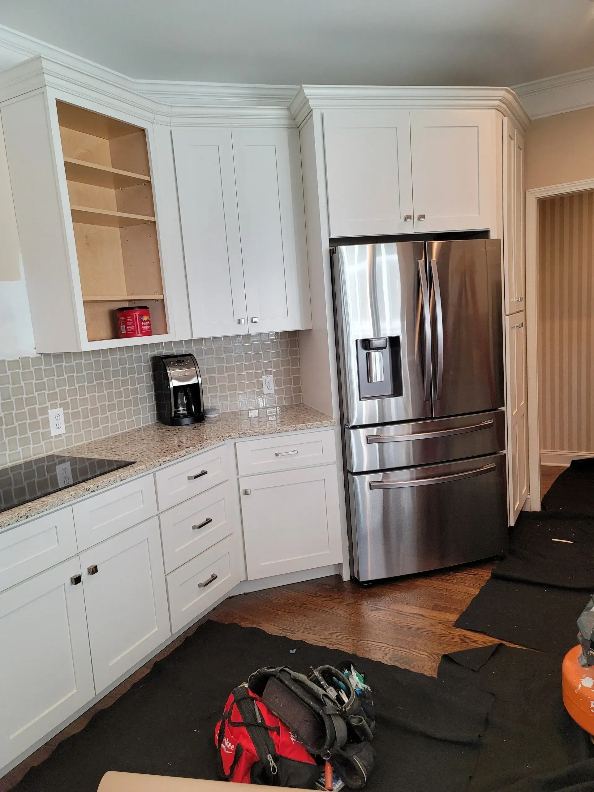 Bright kitchen with white cabinets, stainless steel fridge, coffee maker, and a red-black bag on the floor.