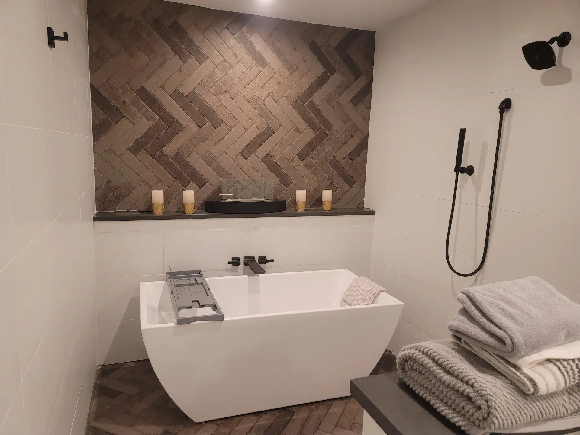 Modern bathroom with freestanding tub, wood accent wall, black shower fixtures, and folded towels on a bench