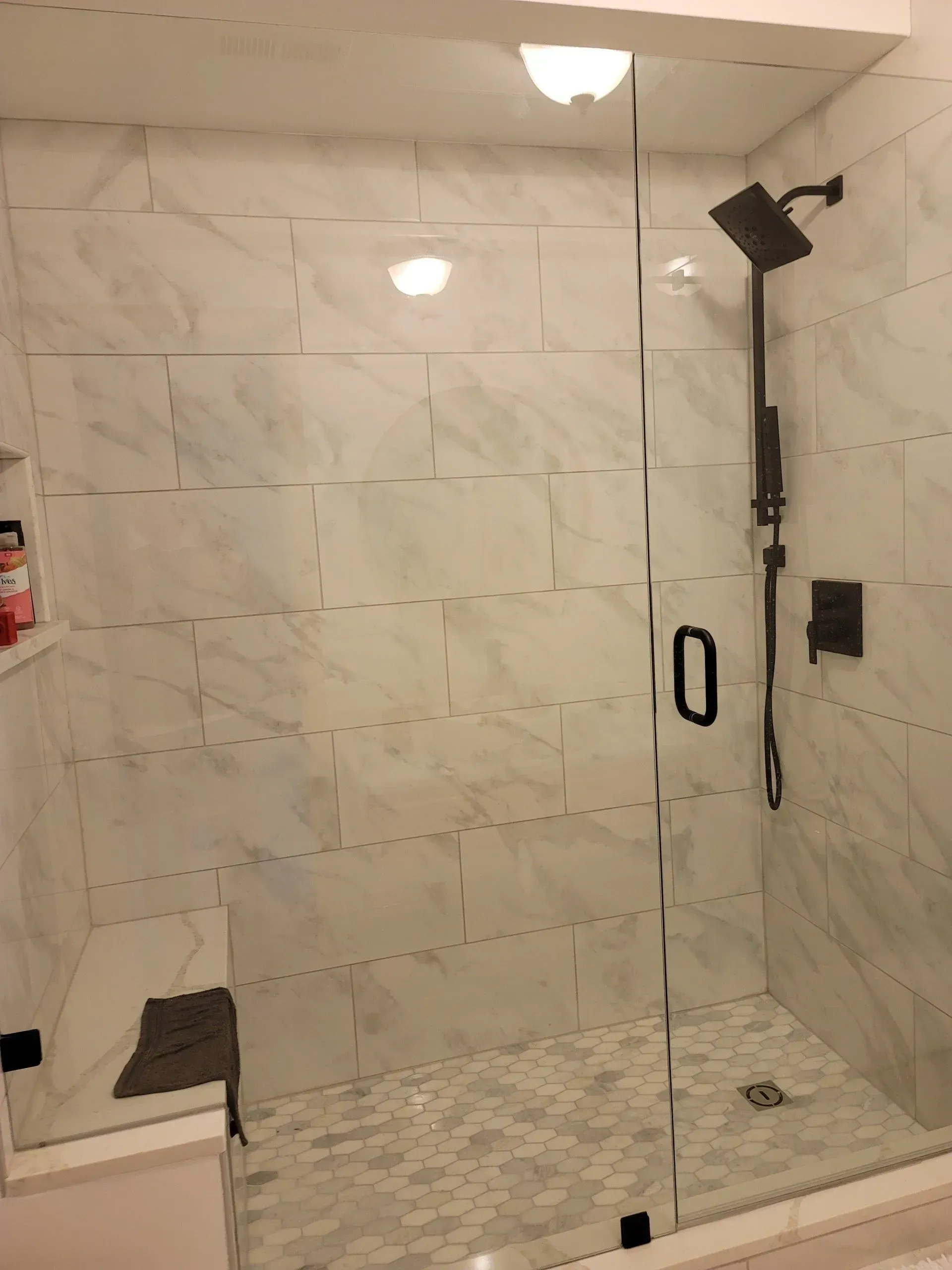 Bathroom shower with marble tile, glass door, and black shower head.