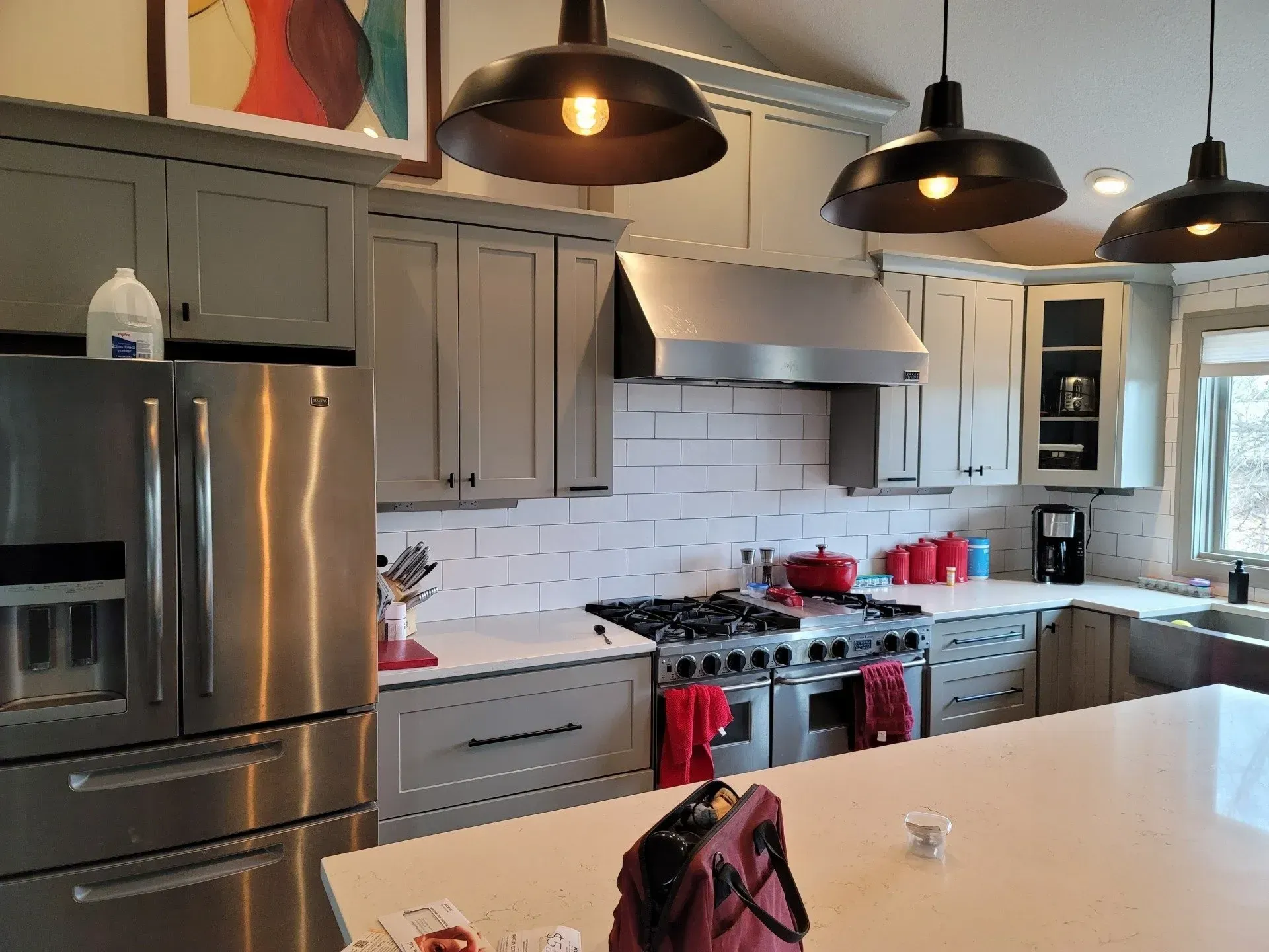 Modern kitchen with gray cabinets, stainless fridge, red stove, and pendant lights over a white island