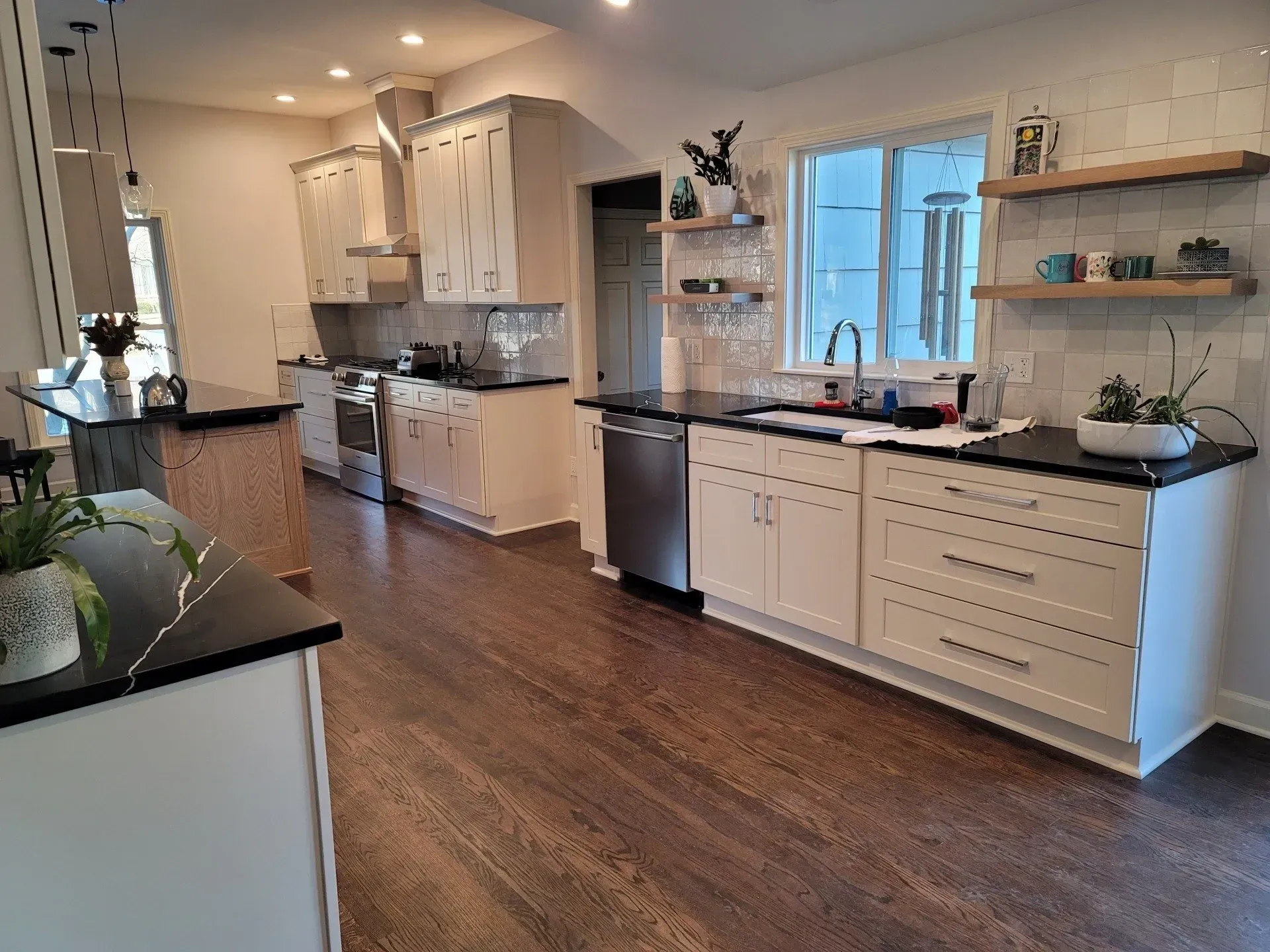 Bright modern kitchen with white cabinets, dark wood floors, island, and large window with shelves.